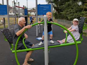 A young boy stands in the middle of a seesaw with a young girl and grandparent at each end
