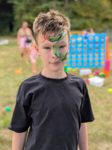 Young boy aged about 8 with a black top on and a snake painted on the left side of his face