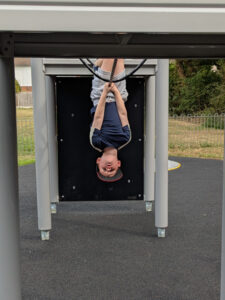 A young boy hangs upside down on the new play equipment