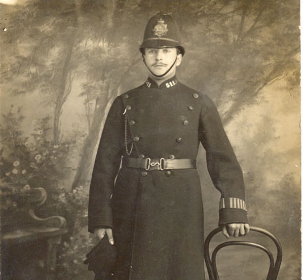 Black and White photo of policeman in uniform standing by a chair