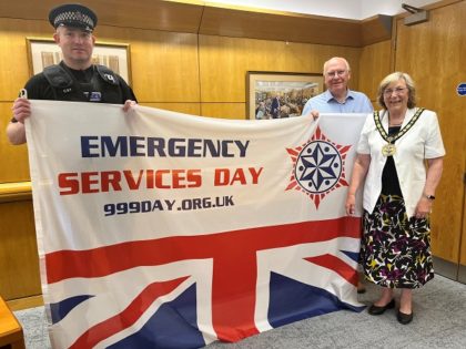Sgt Neil Ross John Sartin and Cllr Mary Sartin holding the emergency services day flag